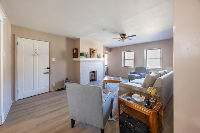 living room with ceiling fan, a fireplace, light wood-type flooring, and baseboards