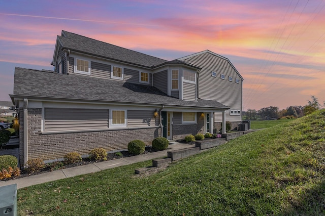 view of front of house with a lawn, brick siding, and a shingled roof