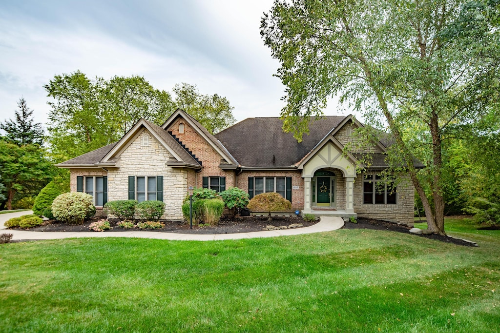 view of front facade with brick siding, stone siding, a shingled roof, and a front yard