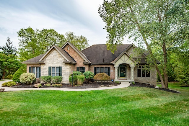 view of front facade with brick siding, stone siding, a shingled roof, and a front yard