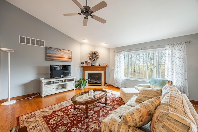 living room featuring a fireplace with flush hearth, wood finished floors, visible vents, vaulted ceiling, and baseboards