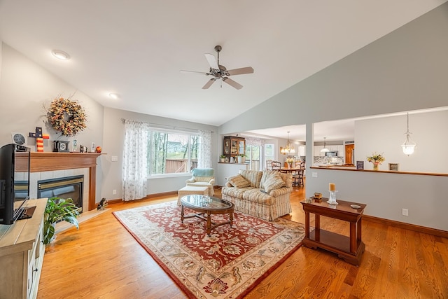 living area featuring lofted ceiling, baseboards, a tiled fireplace, and wood finished floors