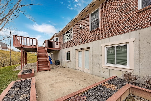 back of house with brick siding, a vegetable garden, a patio area, a wooden deck, and stairs