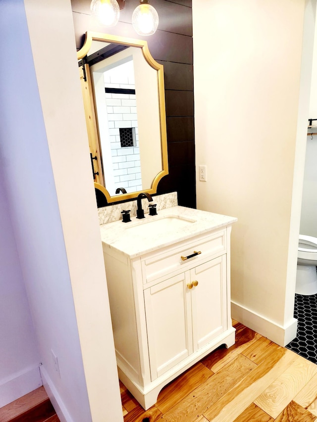 bathroom featuring baseboards, toilet, wood finished floors, and vanity