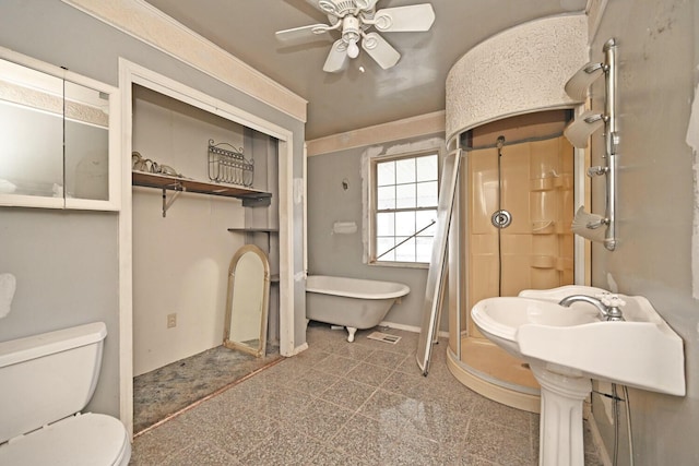 bathroom featuring a soaking tub, toilet, a stall shower, ceiling fan, and baseboards