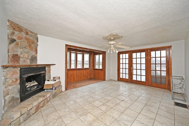 unfurnished living room with a textured ceiling, a fireplace, visible vents, a ceiling fan, and french doors