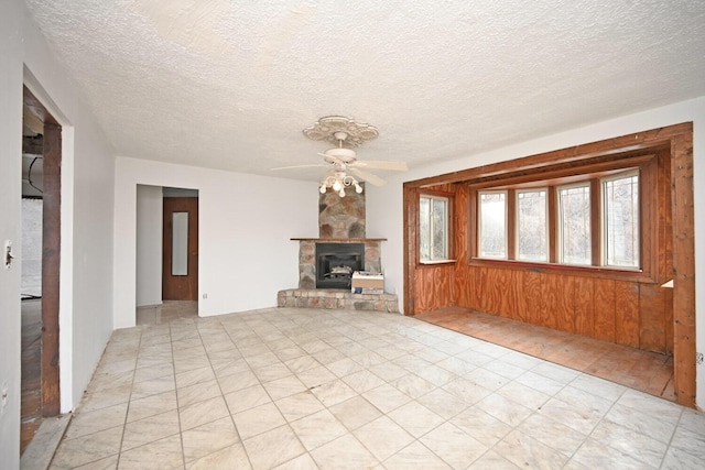 unfurnished living room featuring ceiling fan, wood walls, a fireplace, and a textured ceiling