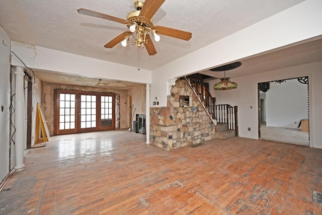 unfurnished living room featuring a textured ceiling, hardwood / wood-style flooring, a ceiling fan, french doors, and stairway