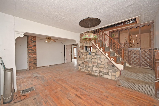 unfurnished living room with visible vents, a ceiling fan, stairway, hardwood / wood-style floors, and a textured ceiling