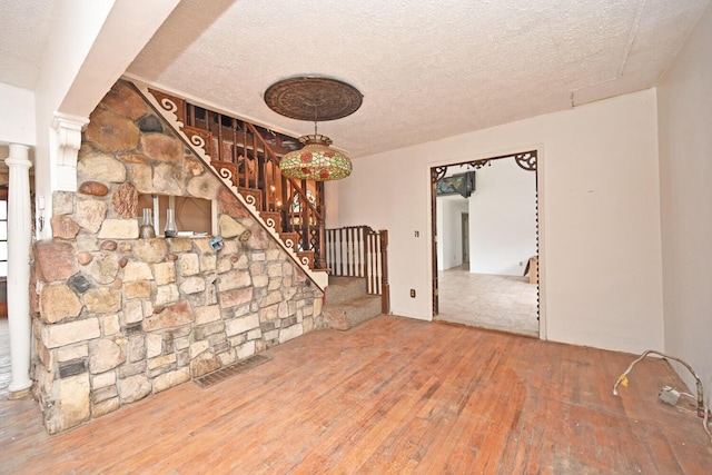 unfurnished living room featuring a textured ceiling, hardwood / wood-style flooring, visible vents, stairway, and decorative columns