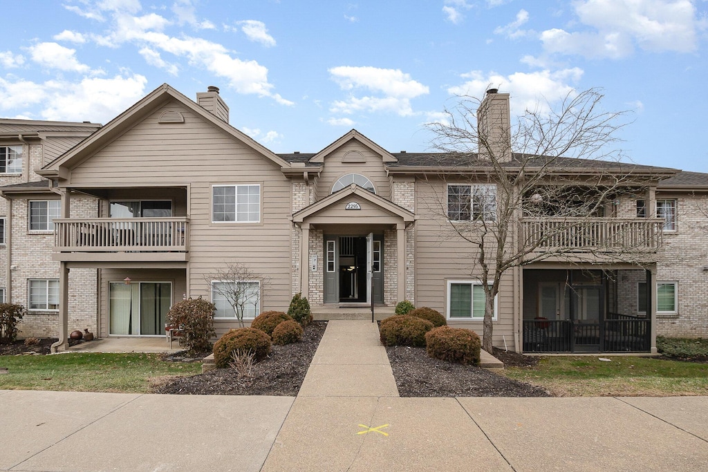 view of front facade featuring brick siding, a chimney, and a balcony