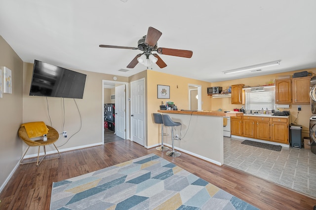 kitchen with a breakfast bar area, a peninsula, baseboards, light wood-style floors, and light countertops