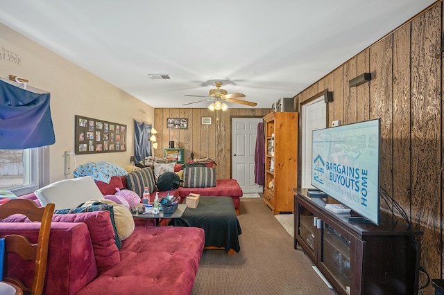 living room featuring ceiling fan, carpet, visible vents, and wooden walls