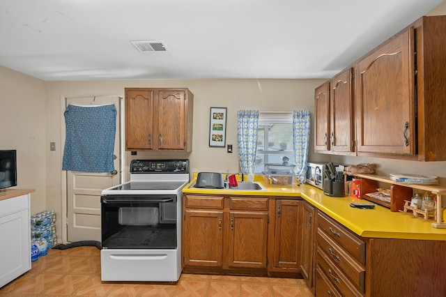 kitchen featuring electric range, visible vents, light countertops, light floors, and brown cabinetry