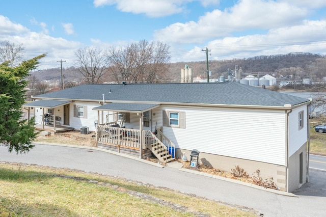 rear view of property with a shingled roof, cooling unit, and covered porch