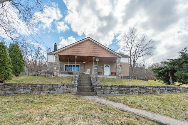 view of front of home with stone siding, ceiling fan, a porch, and a front yard