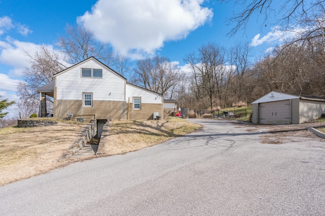 view of property exterior featuring a garage, brick siding, an outdoor structure, and aphalt driveway