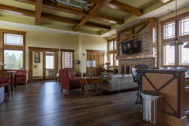 living room with dark wood-type flooring, coffered ceiling, a stone fireplace, and a high ceiling