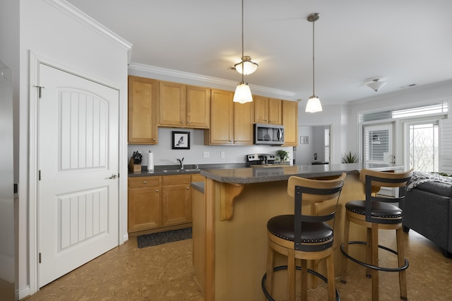 kitchen featuring stainless steel appliances, a breakfast bar, a sink, ornamental molding, and dark countertops