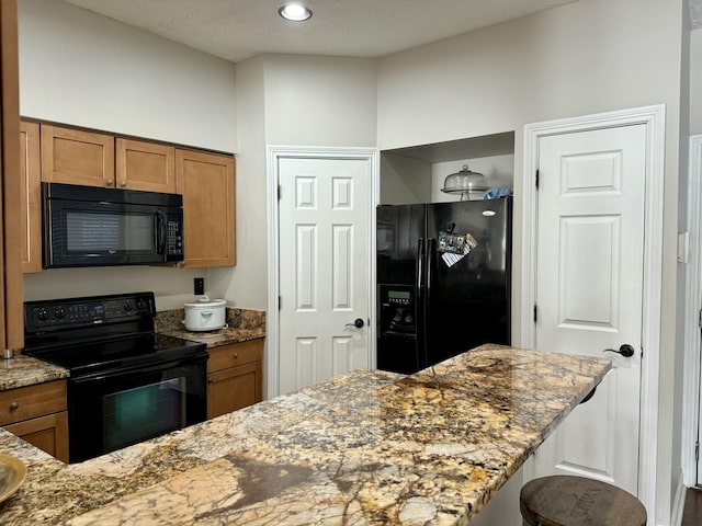 kitchen with a breakfast bar area, brown cabinetry, stone counters, recessed lighting, and black appliances