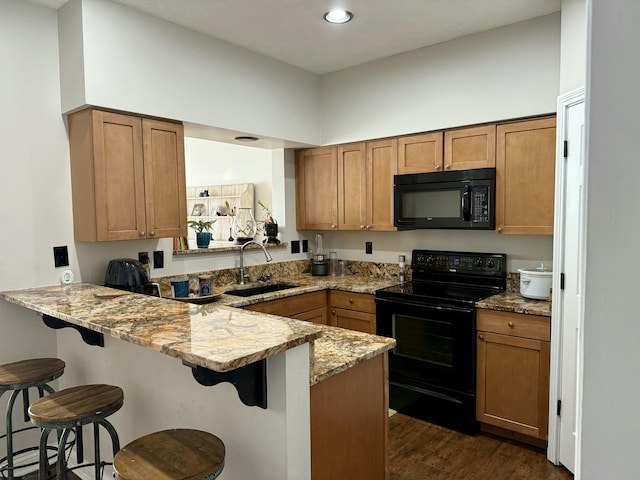 kitchen with a breakfast bar area, a peninsula, brown cabinetry, black appliances, and a sink