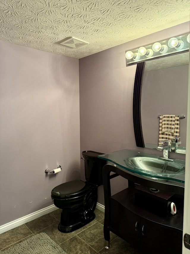 bathroom featuring toilet, baseboards, visible vents, and a textured ceiling