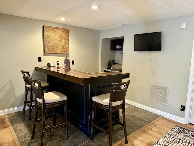 bar featuring visible vents, a dry bar, a textured ceiling, and baseboards