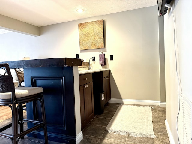 bar featuring a sink, baseboards, wet bar, and a textured ceiling