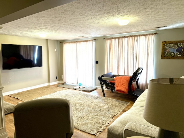 living area featuring visible vents, baseboards, a textured ceiling, and wood finished floors