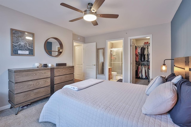 carpeted bedroom with connected bathroom, a walk in closet, baseboards, a closet, and a ceiling fan