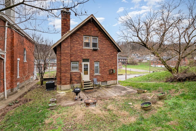 rear view of house with entry steps, central AC, brick siding, a chimney, and a patio area