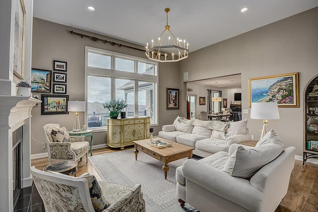 living area featuring baseboards, recessed lighting, a fireplace, wood finished floors, and a notable chandelier