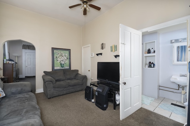 living area featuring tile patterned floors, arched walkways, carpet, and ceiling fan