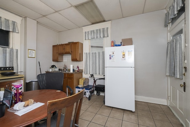 kitchen featuring light tile patterned flooring, a drop ceiling, backsplash, and freestanding refrigerator