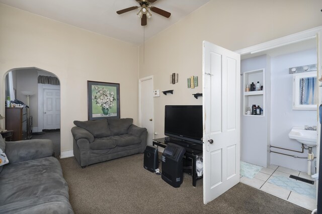 living area featuring tile patterned floors, arched walkways, carpet floors, and a ceiling fan