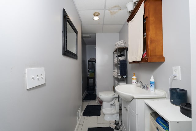 bathroom with tile patterned floors, toilet, a paneled ceiling, and a sink