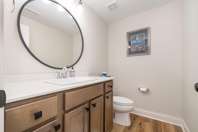 half bathroom with baseboards, visible vents, toilet, wood finished floors, and vanity