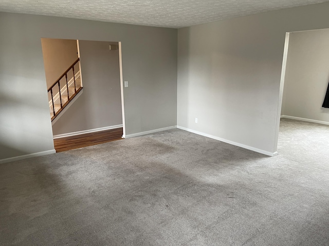 empty room featuring stairs, baseboards, a textured ceiling, and carpet flooring