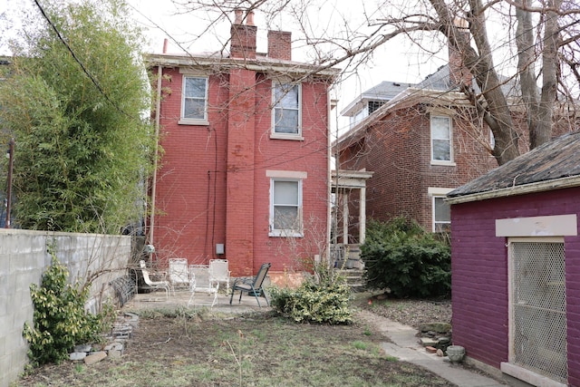 rear view of property featuring brick siding, fence, a chimney, and a patio