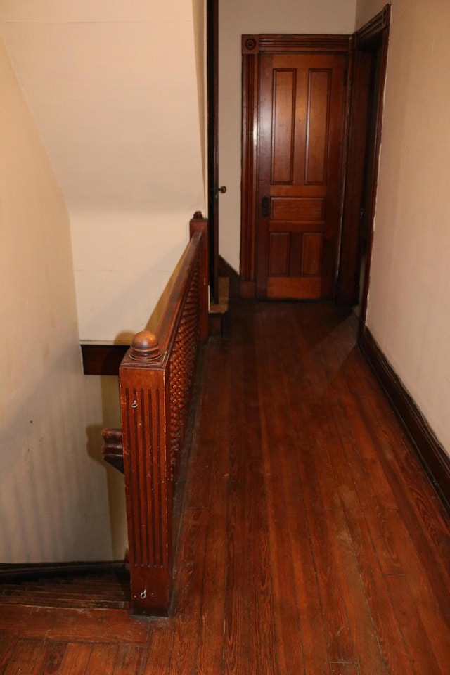 hall featuring radiator, wood-type flooring, baseboards, and an upstairs landing