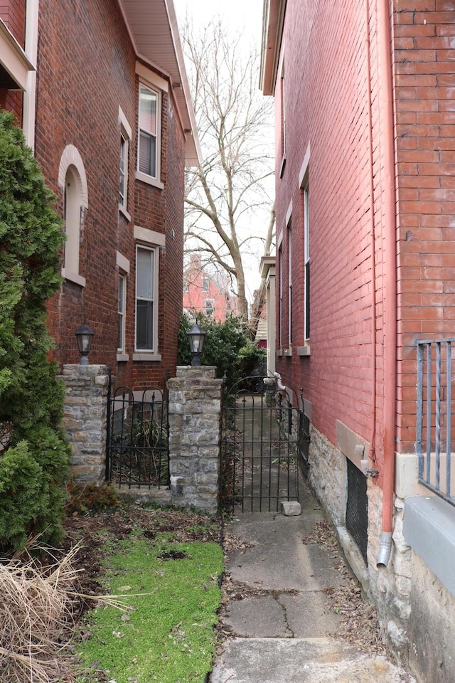 view of side of property with a gate, brick siding, and fence