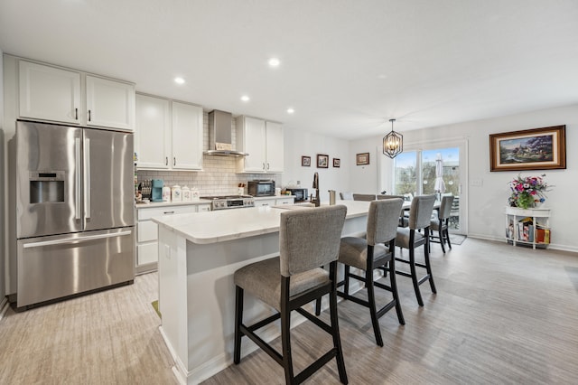 kitchen featuring a center island with sink, stainless steel refrigerator with ice dispenser, a kitchen bar, wall chimney range hood, and backsplash