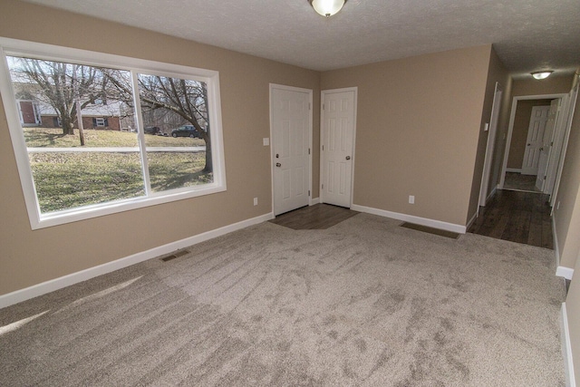 carpeted spare room featuring visible vents, a textured ceiling, and baseboards