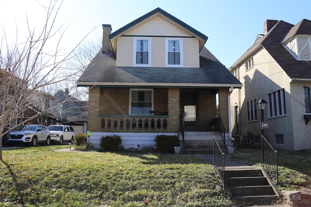 view of front of home featuring brick siding, a porch, a chimney, and a front yard