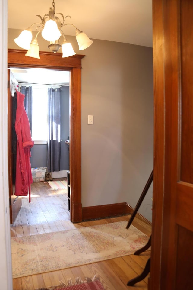 corridor with baseboards, an inviting chandelier, and wood finished floors