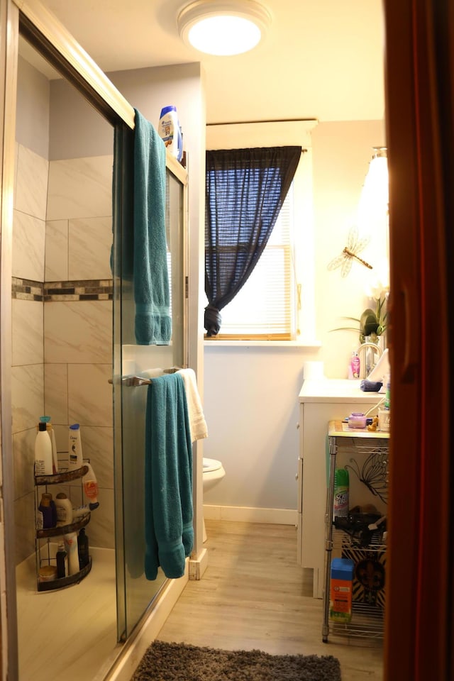 bathroom featuring a shower stall, toilet, wood finished floors, and baseboards