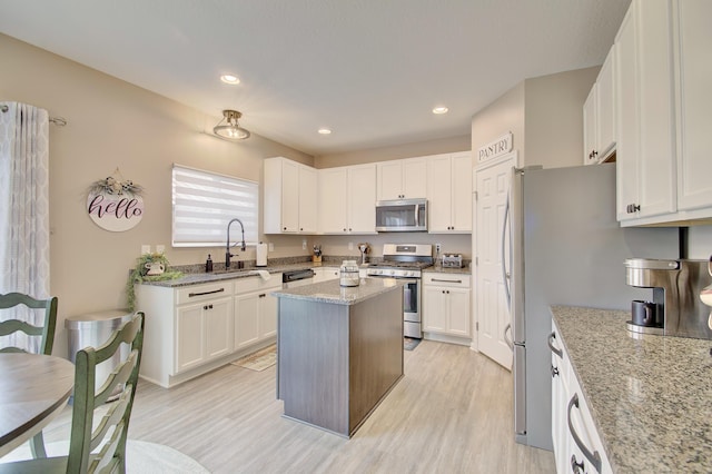 kitchen with white cabinetry, light stone counters, stainless steel appliances, and a sink