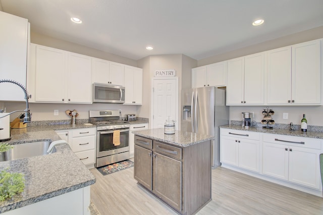 kitchen with white cabinets, light wood-style flooring, appliances with stainless steel finishes, light stone countertops, and a sink