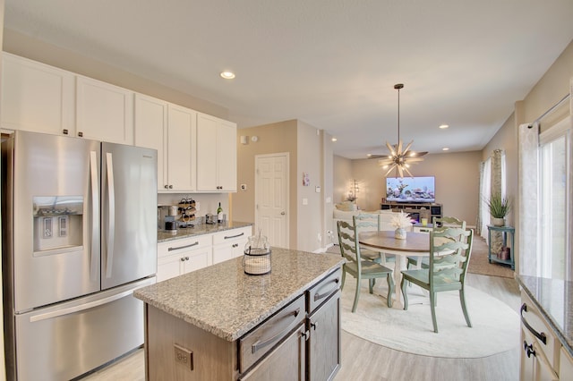 kitchen with light stone counters, light wood-type flooring, open floor plan, and stainless steel fridge