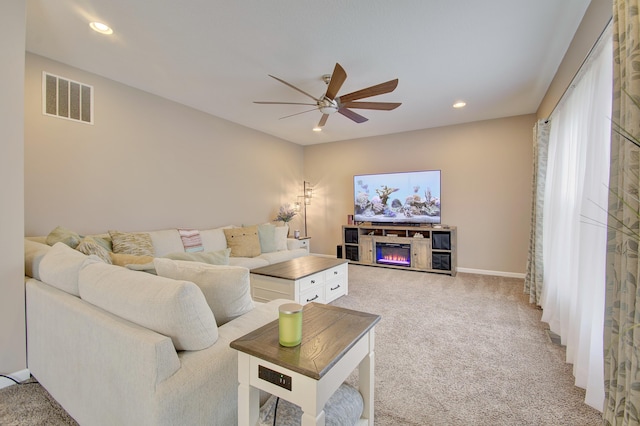 living area featuring recessed lighting, a glass covered fireplace, visible vents, and light colored carpet